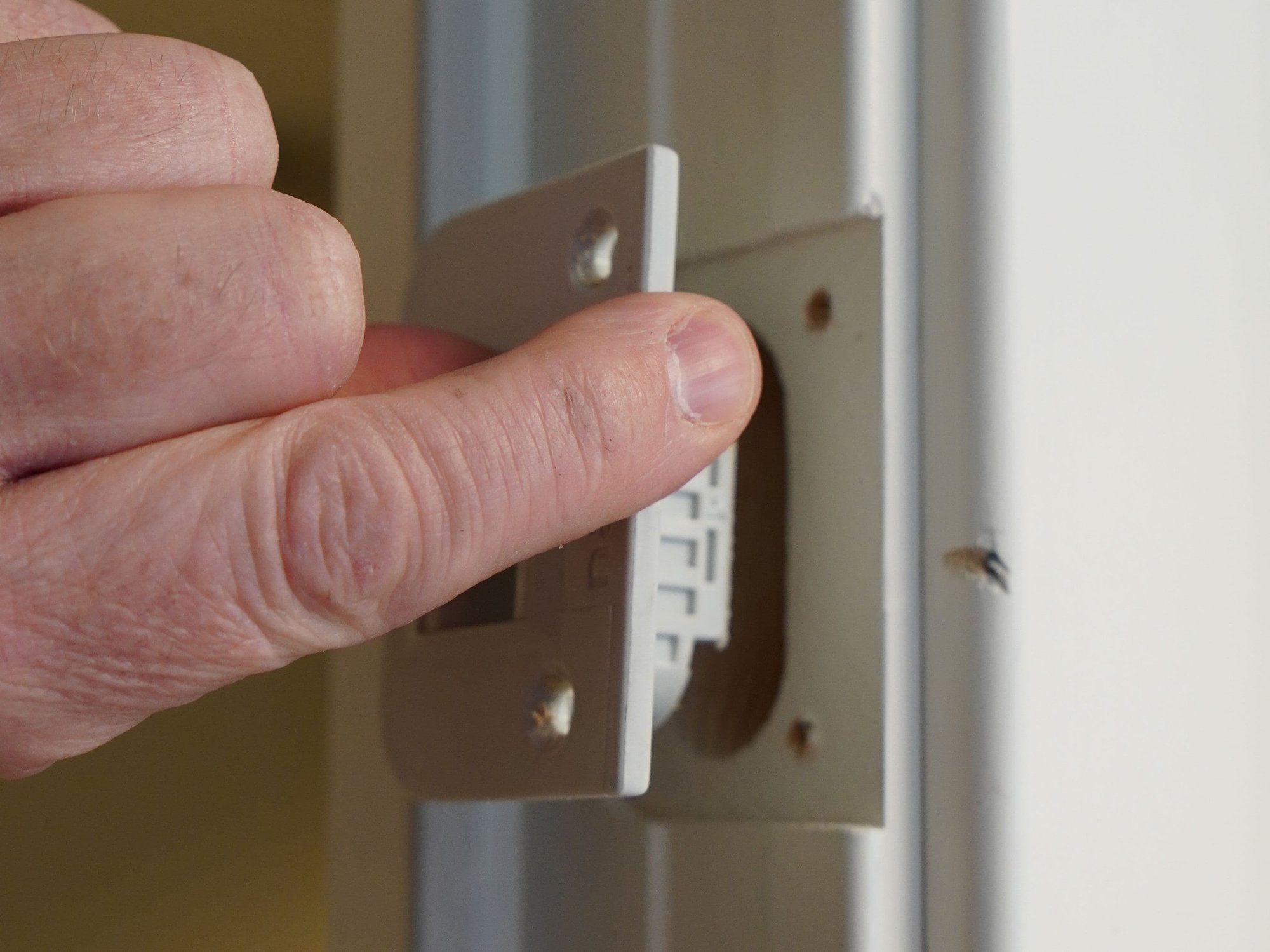 Fingers lift out gray plastic piece in door frame