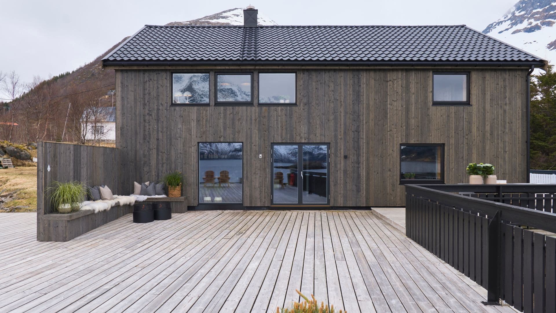 mørkt-hus-med-fjell-bak-og-brygge-foran