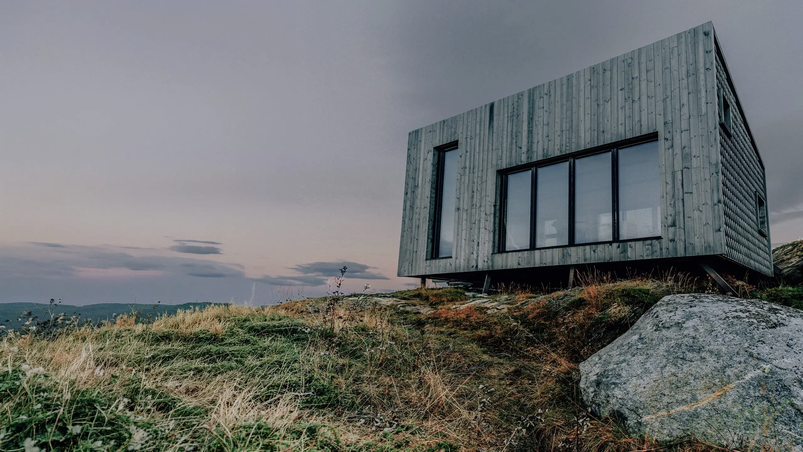 Moderne hytte med trekledning og store vinduer på fjellet.