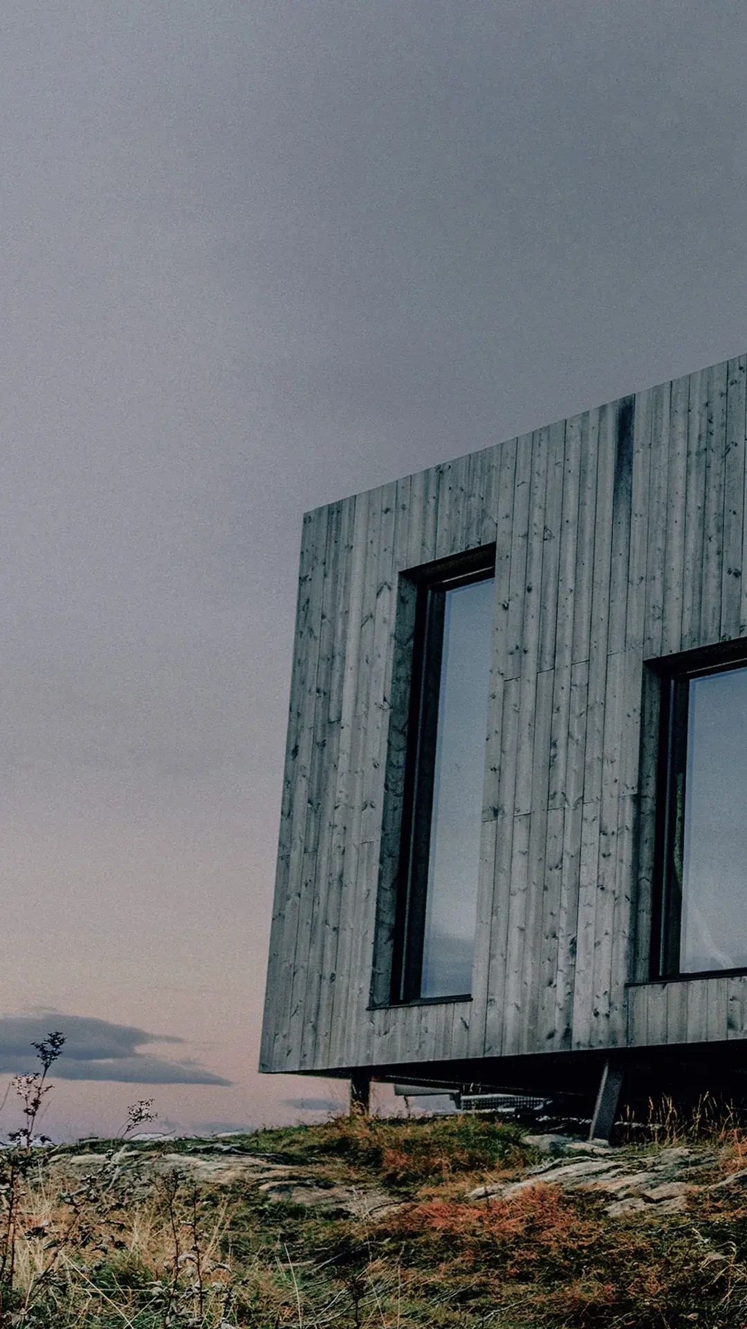 Moderne hytte med trekledning og store vinduer på fjellet.